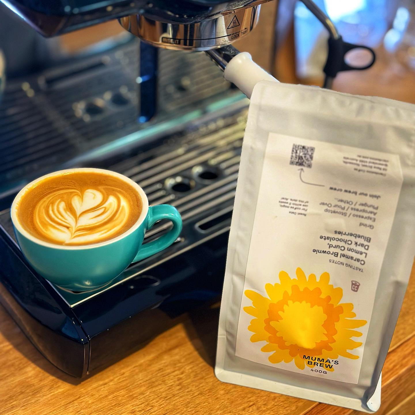 A flat white coffee with latte art sitting on a coffee machine next to a bag of the Clandestino Mummas Brew beans