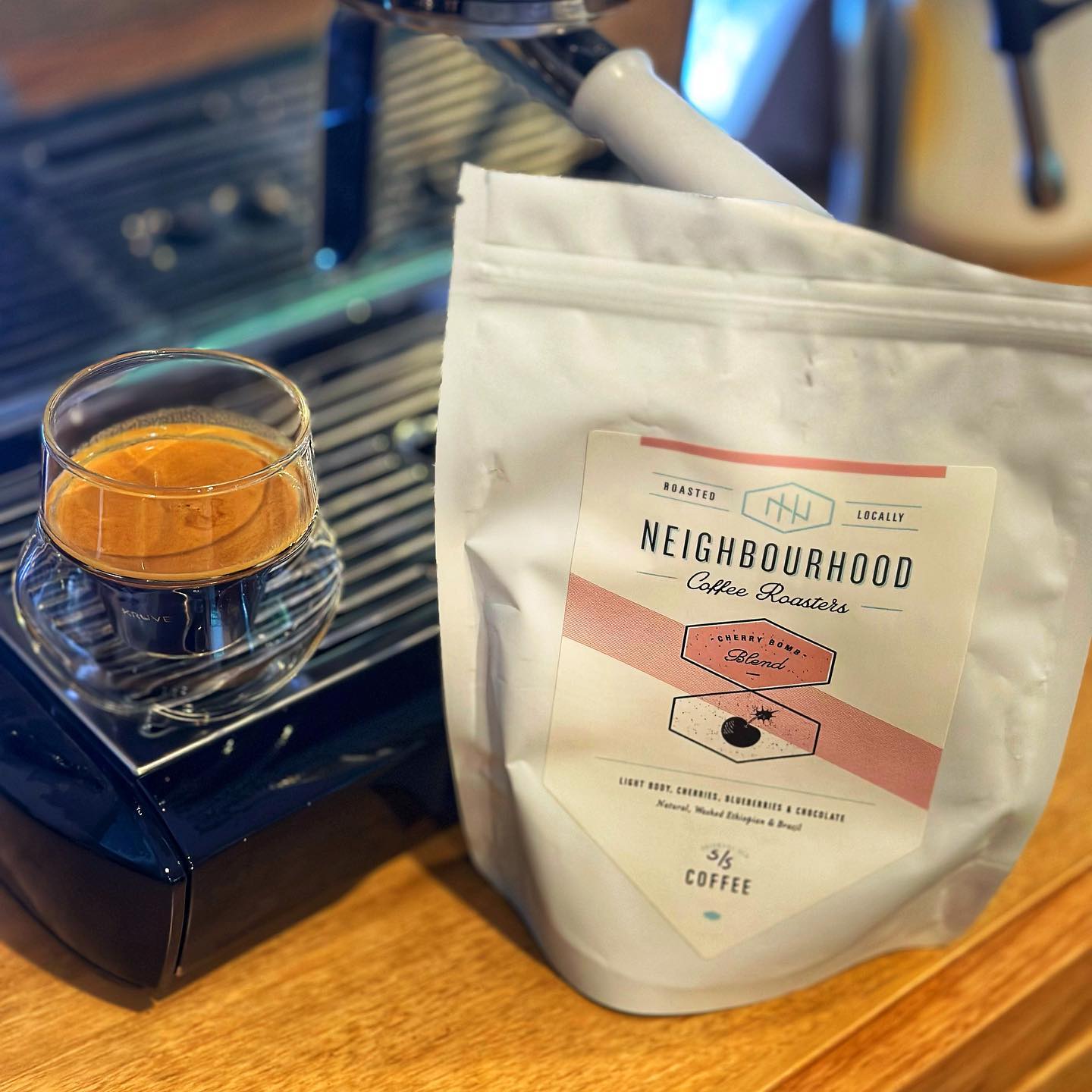 An espresso in a glass sitting on a coffee machine next to a bag of the Neighbourhood Coffee Roasters Cherry Bomb beans