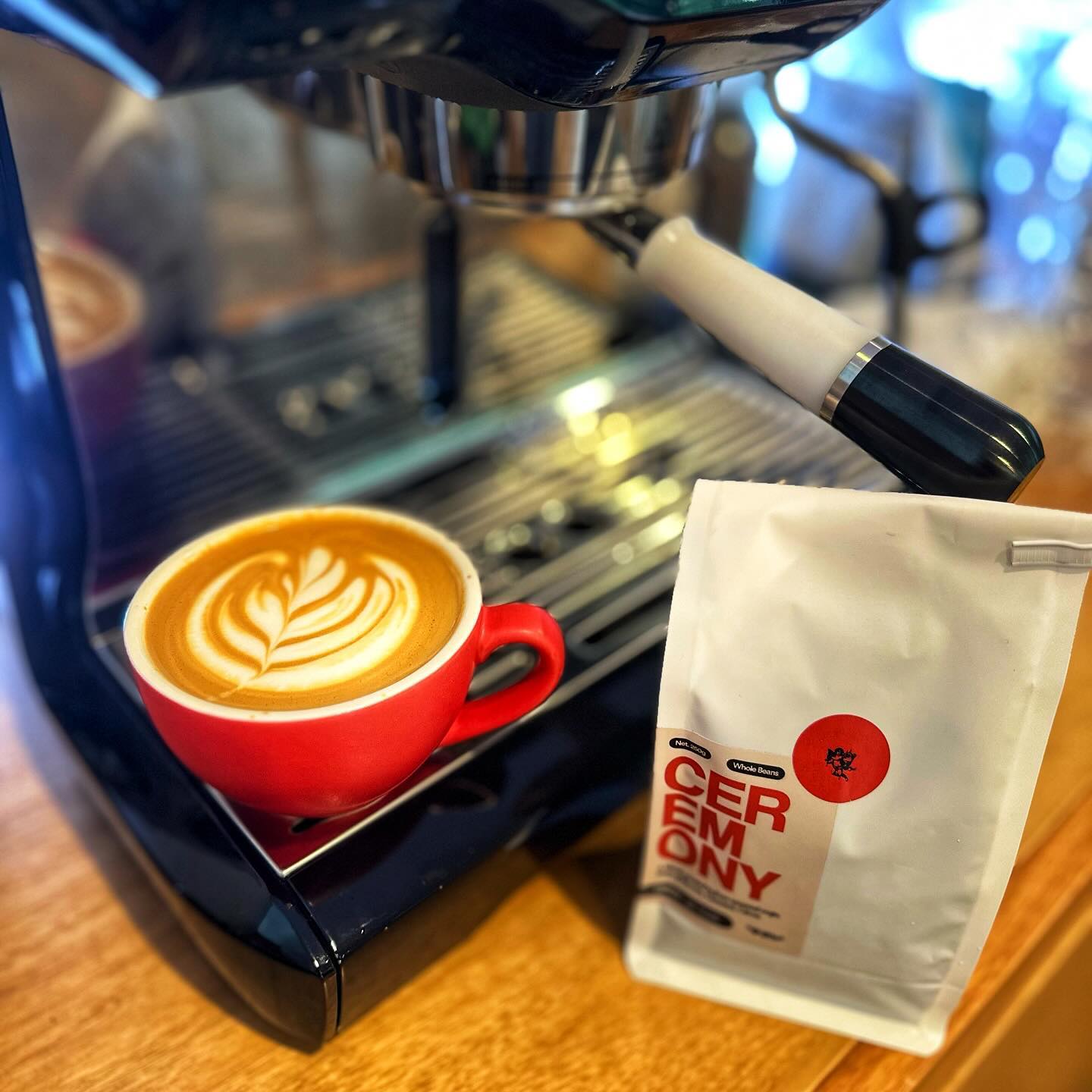 A flat white coffee with latte art sitting on a coffee machine next to a bag of the Omen Coffee Supply Ceremony beans