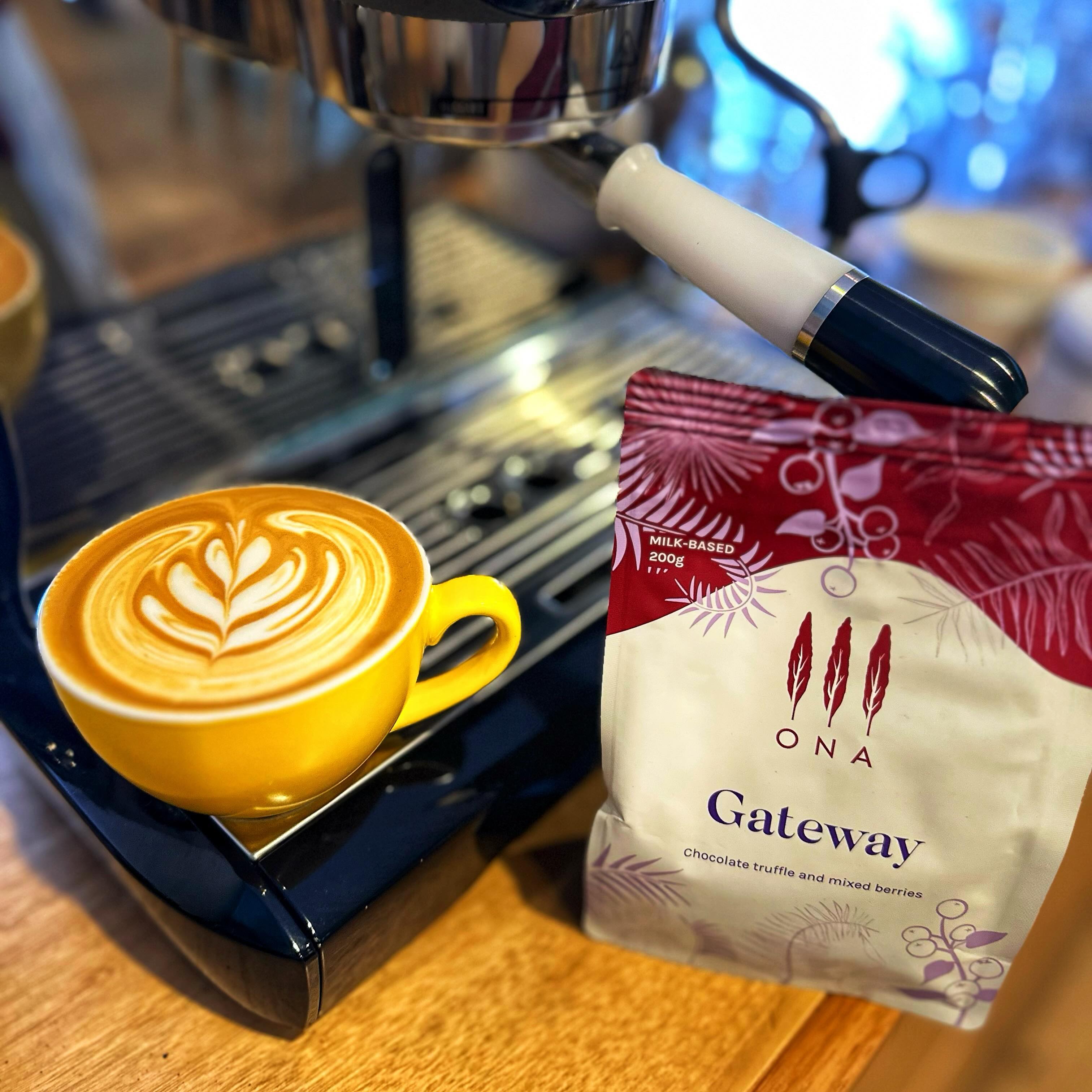 A flat white coffee with latte art sitting on a coffee machine next to a bag of the ONA Gateway coffee beans