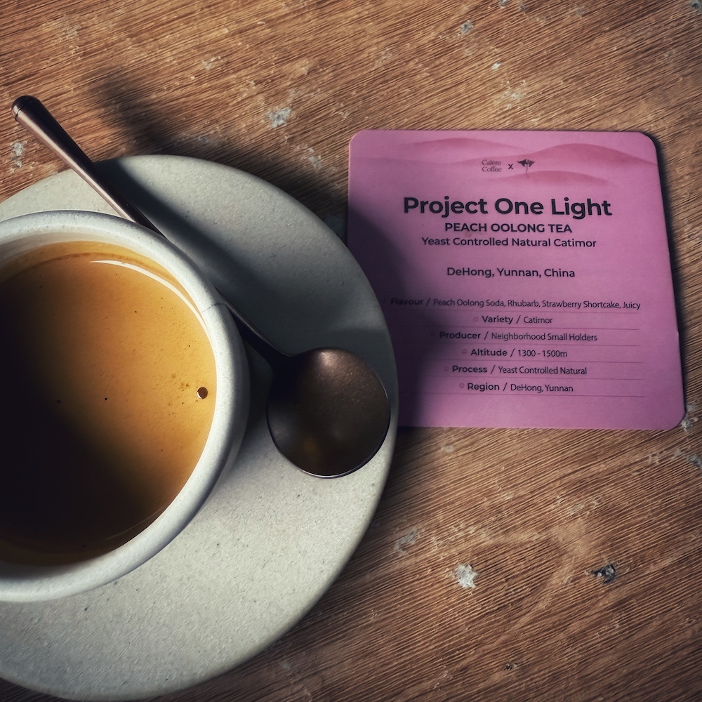 A double espresso in a cup. Next to it is a card with the tasting notes. The coffee is Project One Light - Peach Oolong Tea, a yeast controlled Natural Catimor from DeHong, Yunnan, China