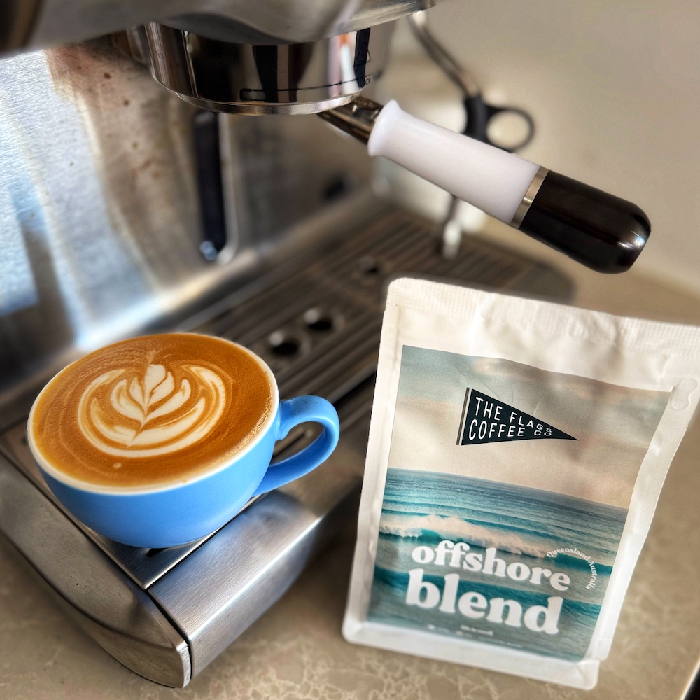 A flat white coffee with latte art on the coffee machine. The bag next to it says The Flag Coffee Co - Offshore Blend