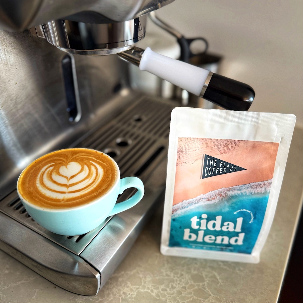 A flat white coffee with latte art on the coffee machine. The bag next to it says The Flag Coffee Co - Tidal Blend