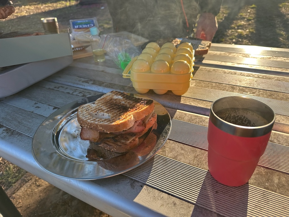 A bacon and egg sandwich and a coffee on a camp table