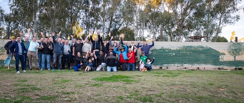 A group shot of all the attendees standing against a corregated iron wall